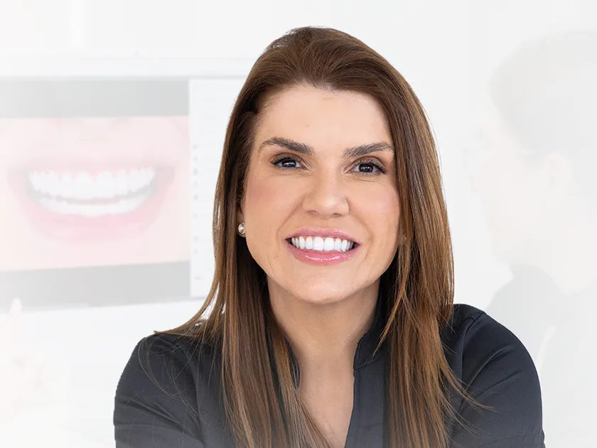 Dra. Gabriela Brum no consultório, olhando para a câmera e sorrindo